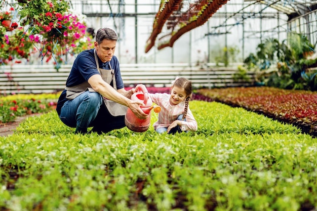 Menina feliz se divertindo enquanto rega as plantas e ajuda o pai no centro de jardinagem