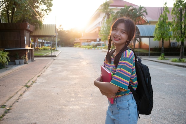 Menina feliz segura livro com mochila andando na escola