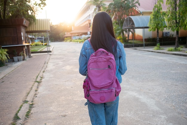 Menina feliz segura livro com mochila andando na escola