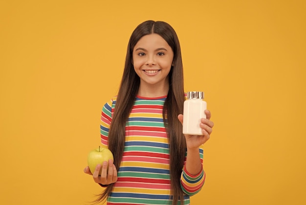 Menina feliz segura maçã e suplemento garrafa de vitaminas de fundo amarelo