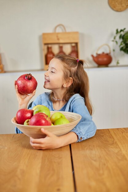 Menina feliz segura tigela com frutas na cozinha em casa lanche infantil saudável Comida saudável em casa adora frutas e vitaminas