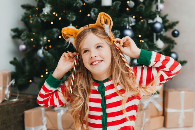 Menina feliz senta-se com doces perto da árvore de Natal. Natal.