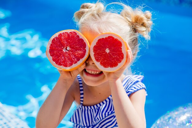 Menina feliz sentada à beira da piscina no verão bebendo limonada