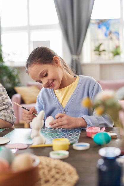 Menina feliz sentada à mesa pintando e decorando ovos para a páscoa em casa