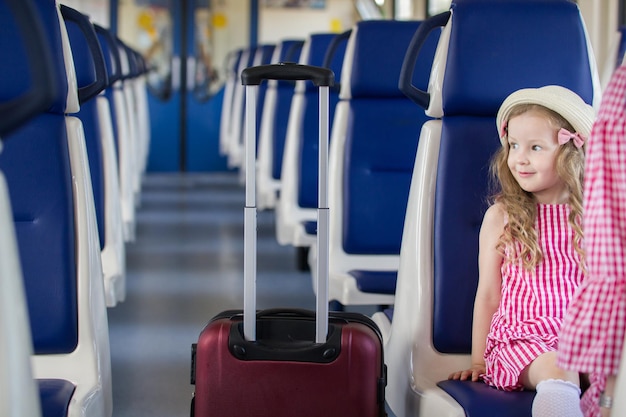 Menina feliz sentada na frente de sua mãe em um vagão de trem vazio, olhando para o lado