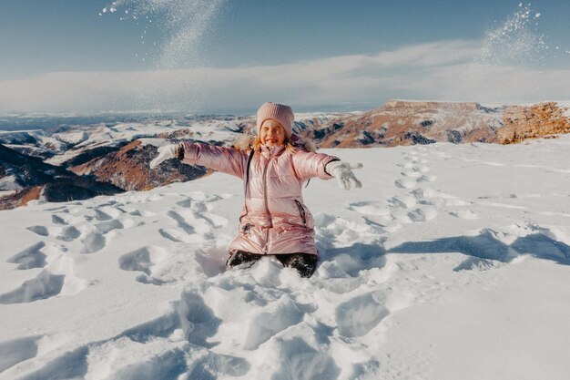 Menina feliz sentada na neve e jogando neve com alegria. conceito de inverno