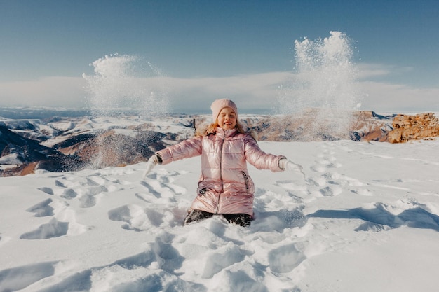 Menina feliz sentada na neve e jogando neve com alegria. conceito de inverno