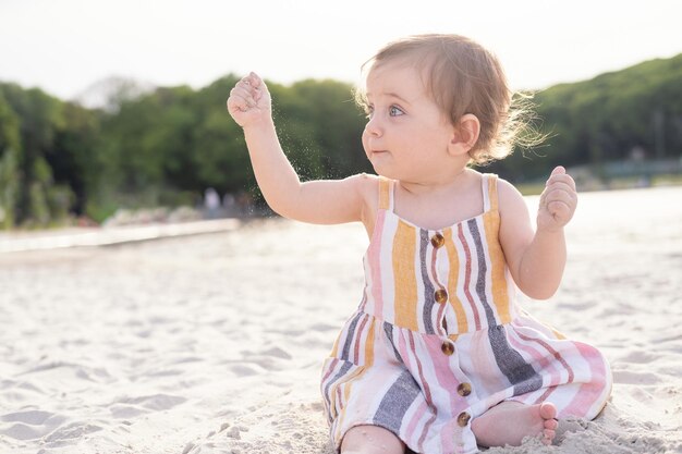 menina feliz sentada na praia na areia usando vestido listrado de verão em dia ensolarado