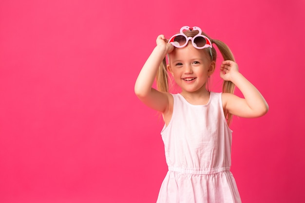 Menina feliz sorrindo em óculos de sol no fundo rosa