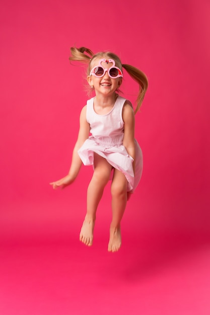 Menina feliz sorrindo em óculos de sol no fundo rosa