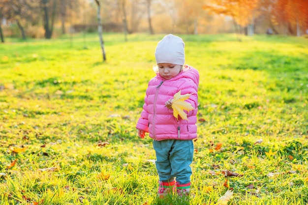 Menina feliz sorrindo no belo parque de outono na natureza caminha ao ar livre Criança brincando com folha de bordo amarela caindo no outono outono fundo amarelo alaranjado Olá conceito de outono