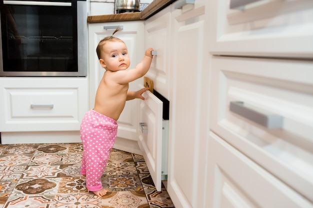 Menina feliz sorrindo sentado na gaveta da cozinha com panelas