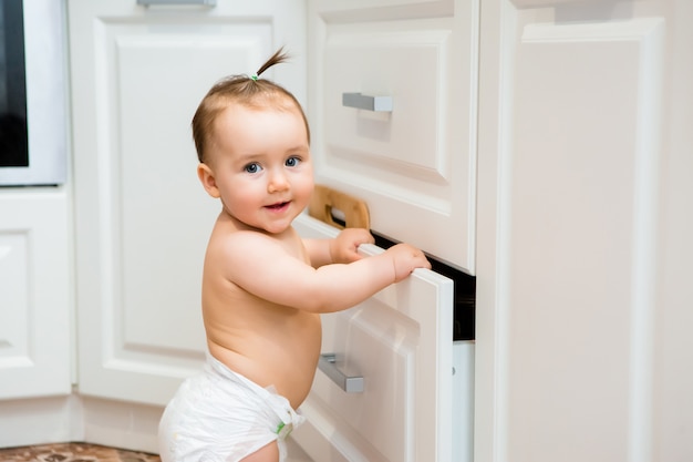 Menina feliz sorrindo sentado na gaveta da cozinha com panelas