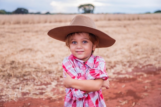 Menina filha de agricultores brincando no jardim alegremente com os braços cruzados Pequena agricultora na fazenda com os braços cruzados