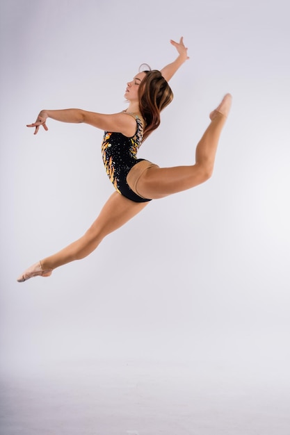 Menina flexível artista de ginástica rítmica pulando na graça de fundo branco escuro em ação de movimento