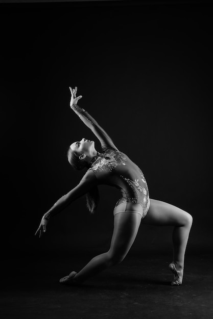 Menina flexível artista de ginástica rítmica pulando na graça de fundo branco escuro em ação de movimento