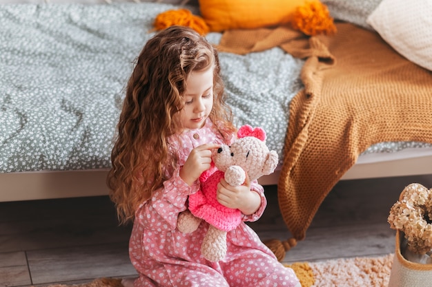 Menina fofa brincando com urso de pelúcia no chão do quarto das crianças