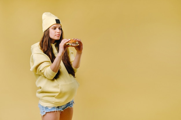 Menina grávida com roupas amarelas e hambúrgueres nas mãos em um fundo amarelo