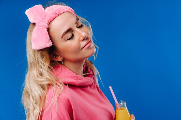 Menina grávida com roupas cor de rosa com uma garrafa de suco em um fundo azul.