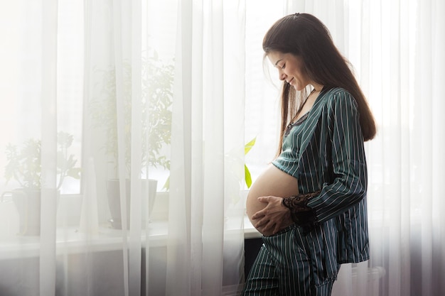 Menina grávida de pijama ao lado da janela