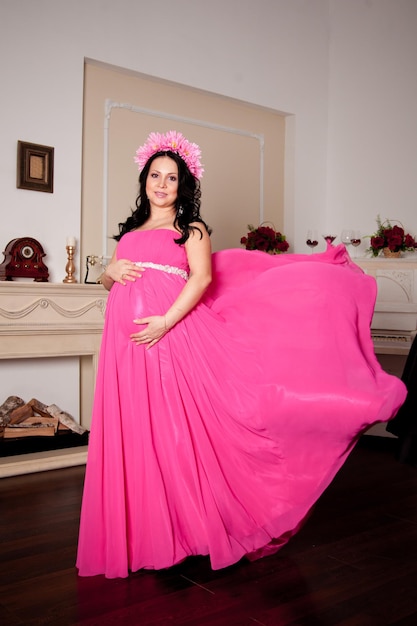 Menina grávida em um vestido rosa com flores no cabelo