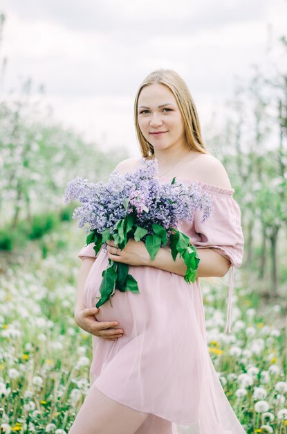 Menina grávida em um vestido rosa em um jardim de flores segurando um lilás