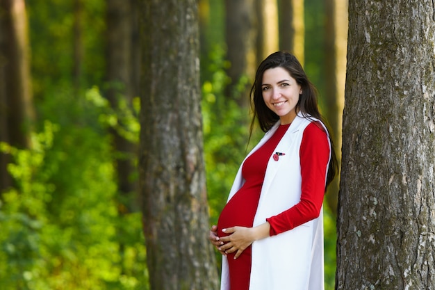 Menina grávida no vestido vermelho. retrato de mulher grávida bonita no vestido vermelho no parque primavera floração