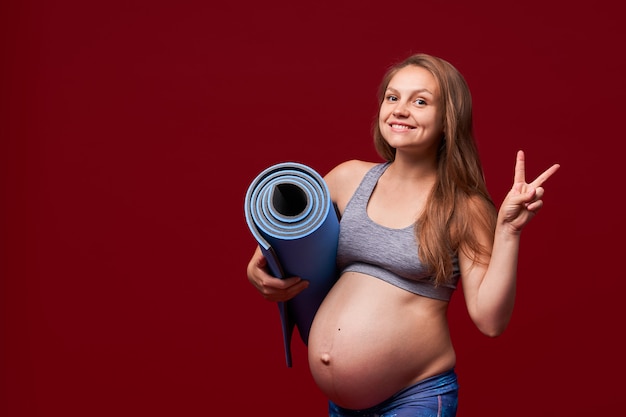 Menina grávida segurando um tapete de esportes nas mãos dela