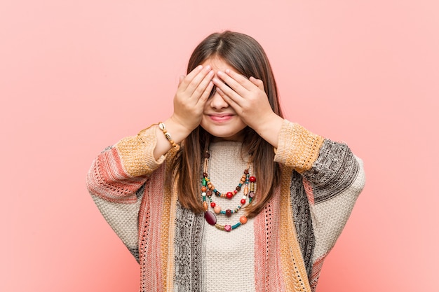 Foto menina hippie cobre os olhos com as mãos, sorri amplamente à espera de uma surpresa.