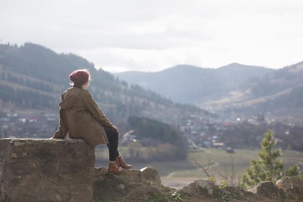 Menina hipster senta-se no fundo das montanhas