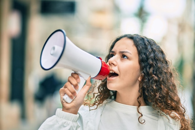 Menina hispânica gritando com raiva usando megafone na cidade