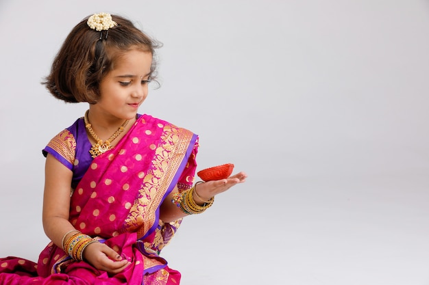 Menina indiana / asiática pequena bonito no desgaste tradicional que guarda uma lâmpada de óleo do diya ou da terracota no festival de Diwali.