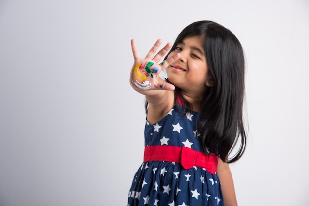 Menina indiana bonitinha mostrando suas mãos coloridas ou impressão palmar ou pintando ou jogando festival de holi com cores, isolado sobre fundo branco