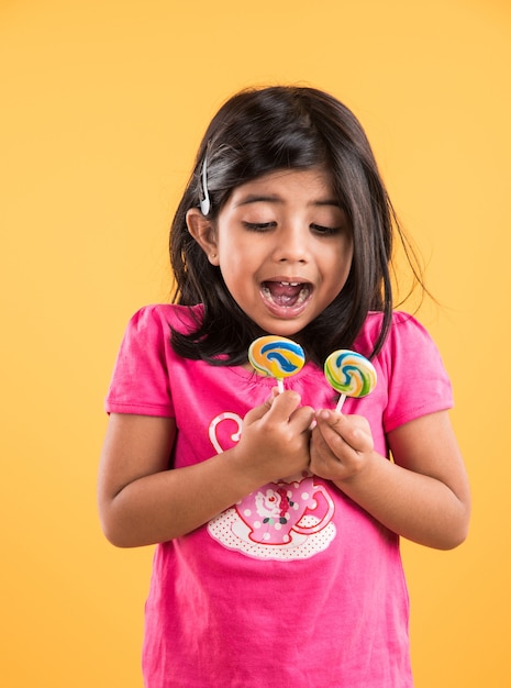 Menina indiana com pirulito ou loly pop, menina asiática e pirulito ou pirulito, garota indiana brincalhona e fofa posando com pirulito ou doce