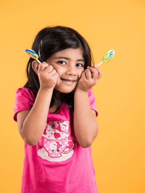 Menina indiana com pirulito ou loly pop, menina asiática e pirulito ou pirulito, garota indiana brincalhona e fofa posando com pirulito ou doce