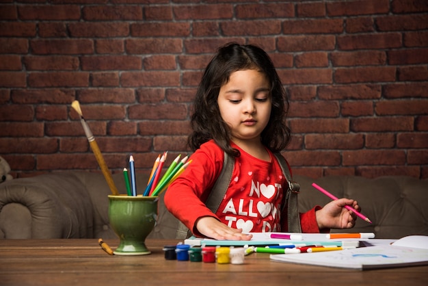 Menina indiana desenhando ou pintando com cores sobre papel, foco seletivo