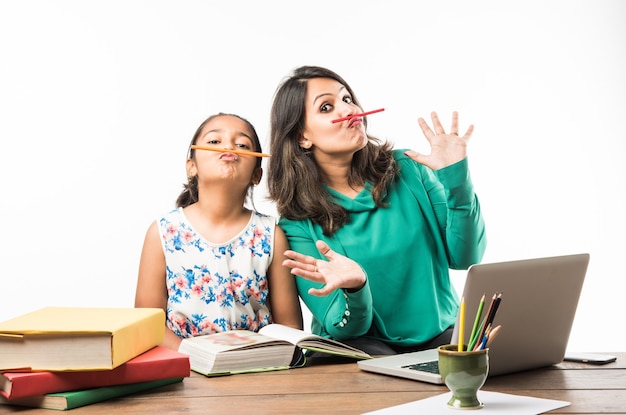 Menina indiana estudando com a mãe ou professora na mesa de estudo com o laptop, livros e se divertindo aprendendo