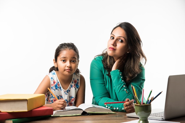 Menina indiana estudando com a mãe ou professora na mesa de estudo com o laptop, livros e se divertindo aprendendo