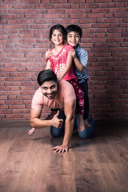 Menina indiana feliz e menino brincando nas costas ou nas costas com o pai, foto interna com a mãe olhando