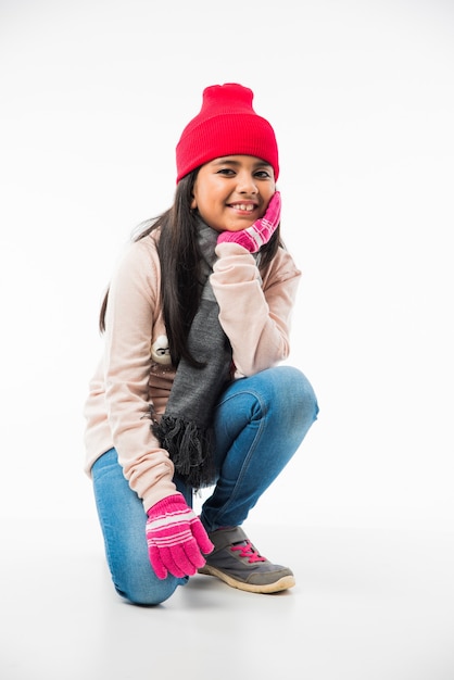 Foto menina indiana fofa com roupas de inverno, de pé contra um fundo branco