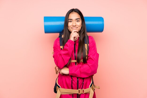 Menina indiana jovem alpinista com uma mochila grande na parede rosa rindo