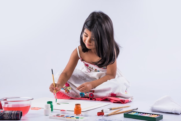 Menina indiana ou asiática bonitinha apreciando a pintura em casa com papel, cor de água e pincel de arte. Foco seletivo