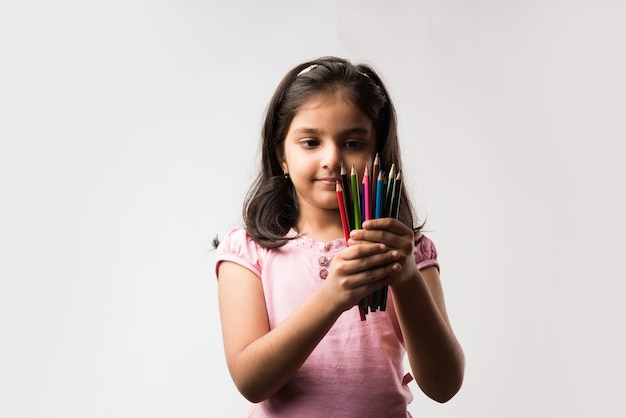 Menina indiana ou asiática bonitinha segurando um lápis de cor, isolada sobre um fundo branco