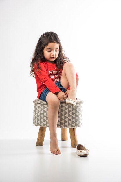 Menina indiana usando sapatos enquanto está sentada em um banquinho, isolado sobre um fundo branco