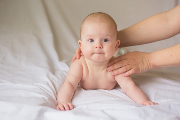 Menina infantil feliz fazendo massagem de bebê por sua mãe em casa. Criança recém-nascida com cerca de 5 meses de idade