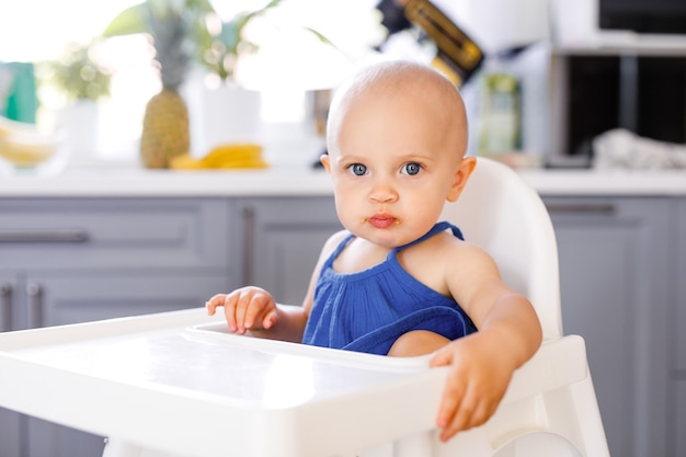 Menina infantil sentada na cadeira de criança alta em um fundo branco. Conceito de comida para bebé, espaço para texto