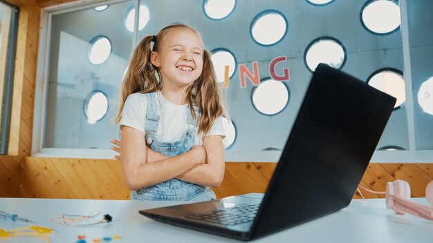 Menina inteligente e bonita usando laptop enquanto olha e ri da câmera Erudição