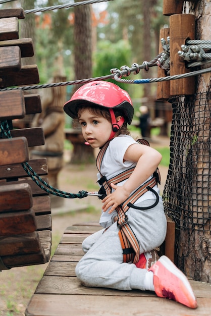 Menina interessada em um capacete protetor, a seguradora está se divertindo no parque de cordas. Criança ativa em um parque de cordas