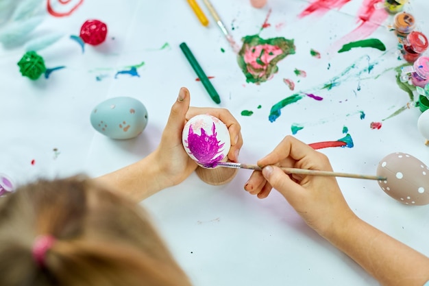 Menina irreconhecível pintando desenho com ovos de pincel em casa