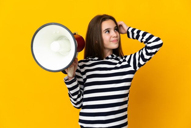 Menina isolada em fundo amarelo segurando um megafone e tendo dúvidas